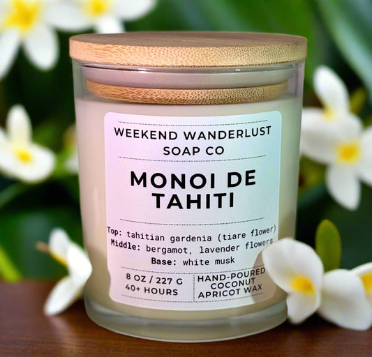 Candle jar labeled 'Monoi de Tahiti' from Weekend Wanderlust Soap Co with flowers around it.