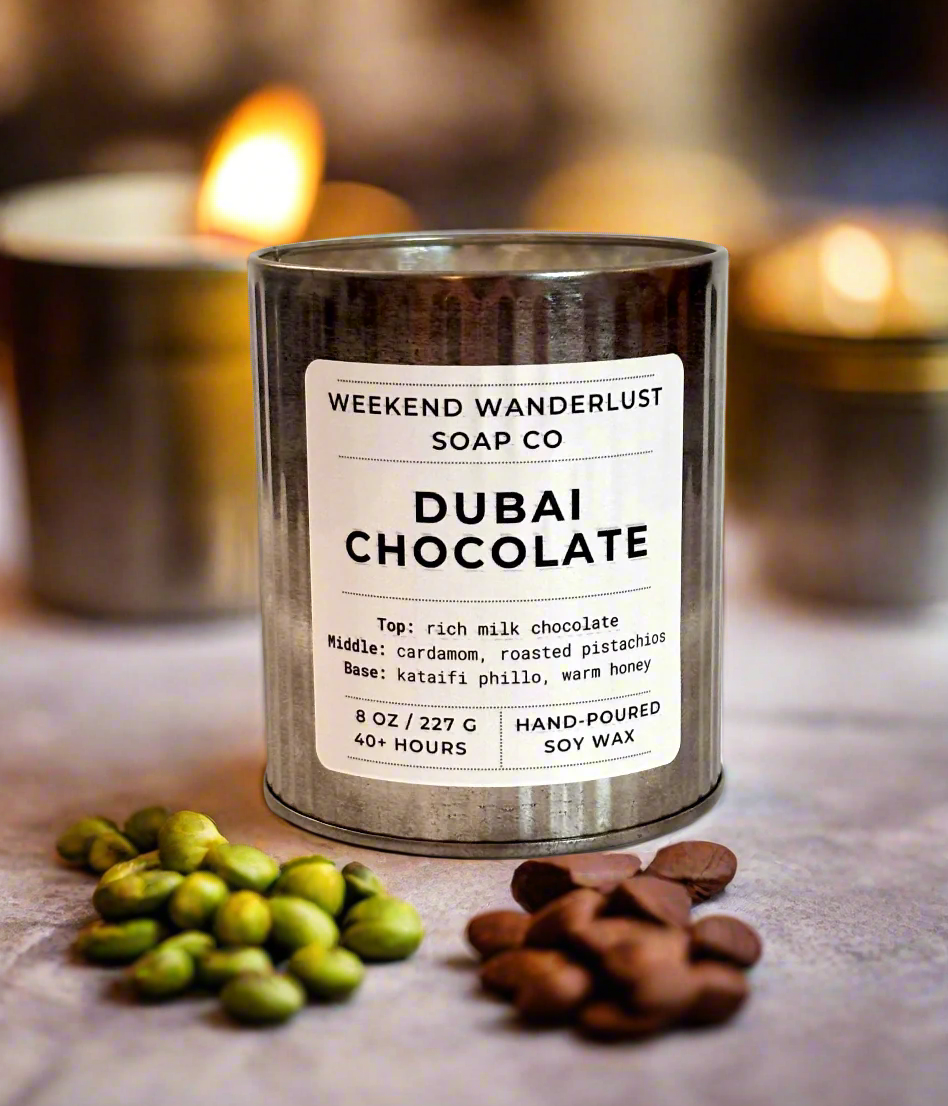 Candle labeled 'Dubai Chocolate' from Weekend Wanderlust Soap Co with green beans and chocolate chips on a surface.