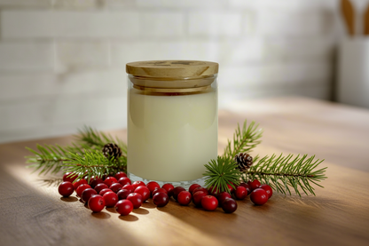 Candle with wooden lid surrounded by red berries and greenery on a wooden surface