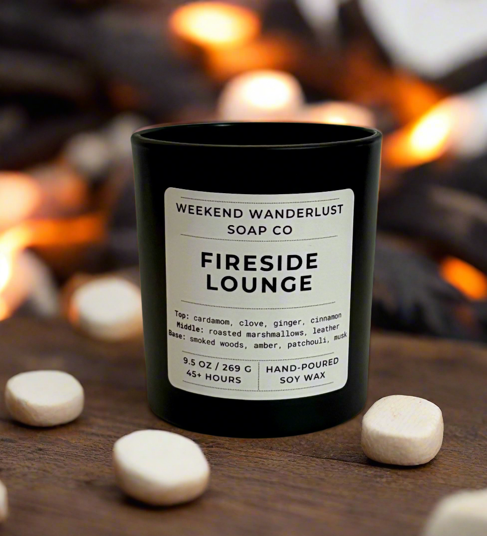 Candle labeled 'Fireside Lounge' from Weekend Wanderlust Soap Co. on a wooden surface with a fireplace in the background.