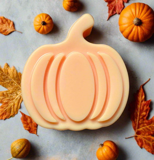 Pumpkin-shaped soy wax melt with autumn leaves and small pumpkins on a gray surface