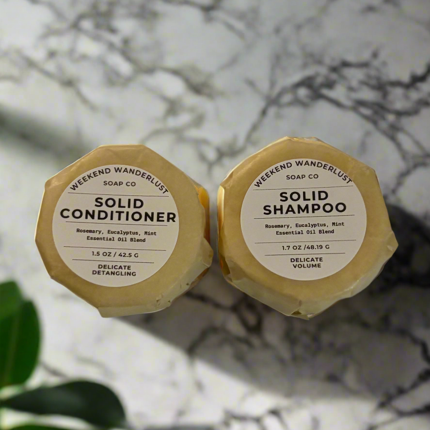 Two solid shampoo and conditioner bars with labels on a marble surface.