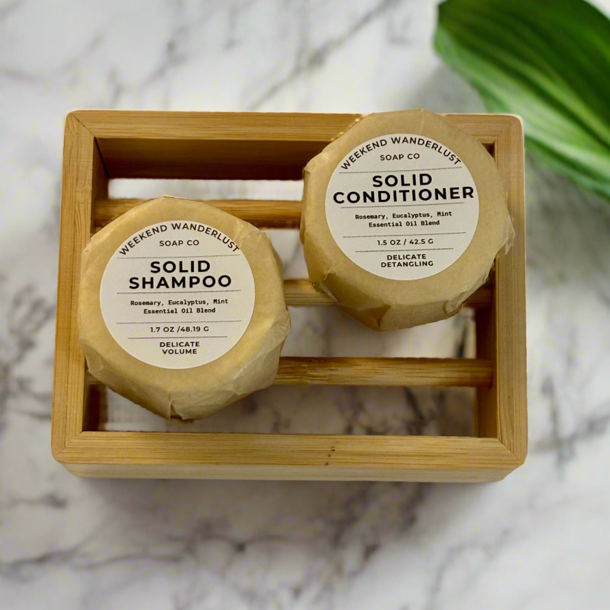 Two solid shampoo and conditioner bars in a wooden tray on a marble surface.
