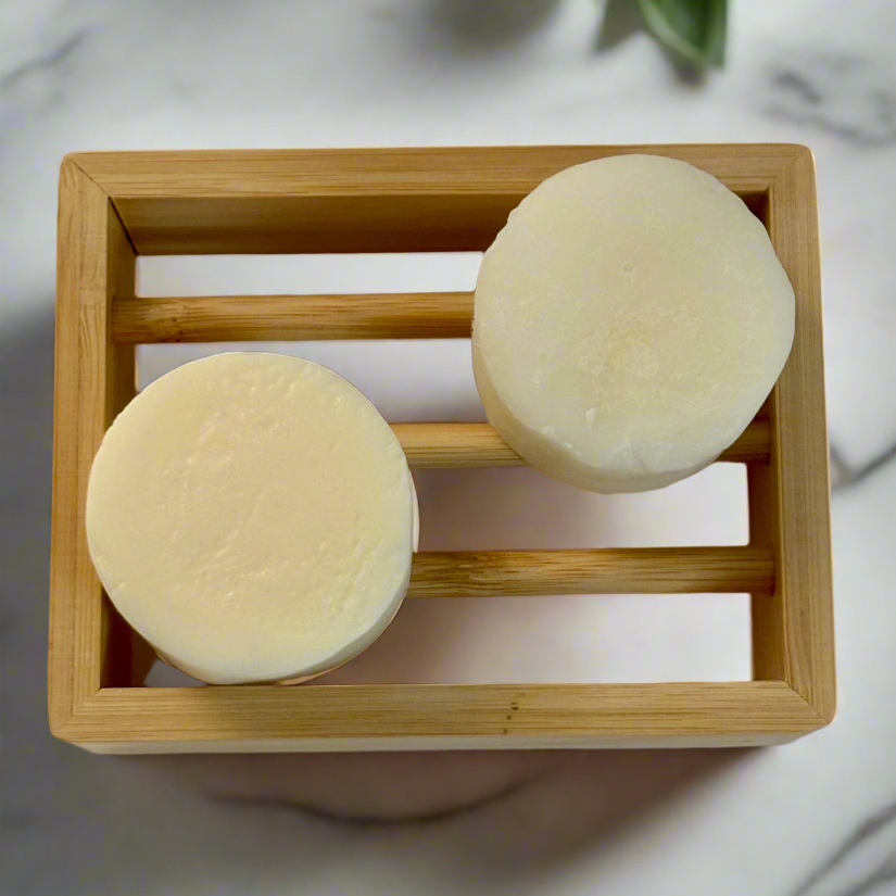 Two round beige bars of soap on a square wooden soap dish with a marble background.