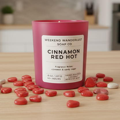 candle labeled 'Cinnamon Red Hot' from Weekend Wanderlust Soap Co on a wooden surface with red candies.